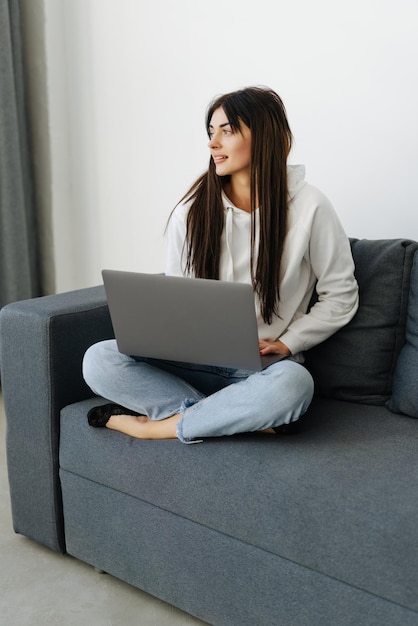 Glückliche Frau, die einen Laptop verwendet, der auf einem gemütlichen Sofa sitzt