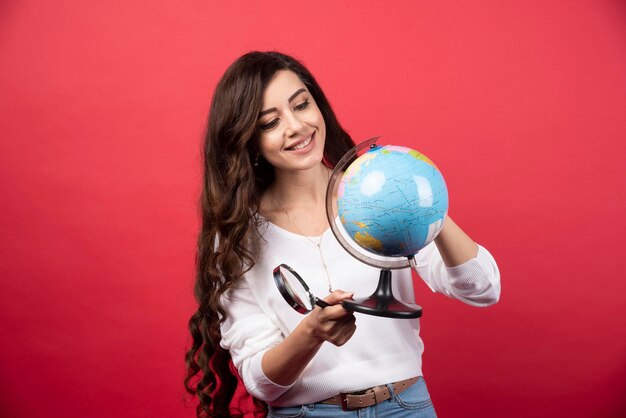 Glückliche Frau, die Globus auf rotem Hintergrund betrachtet. Foto in hoher Qualität