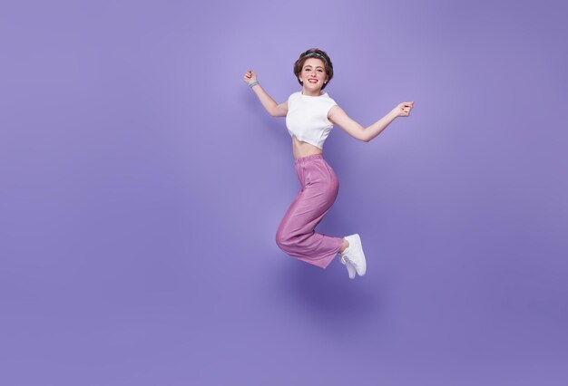 Glückliche Frau, die lächelt und springt, während sie den Erfolg feiert, isoliert auf violettem Hintergrund