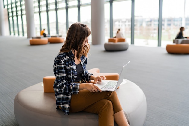 Glückliche Frau, die Laptop beim Sitzen am Flughafenlounge verwendet.