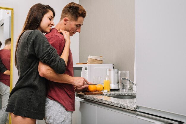 Glückliche Frau, die Mann von hinten umarmt, während er Orange schneidet