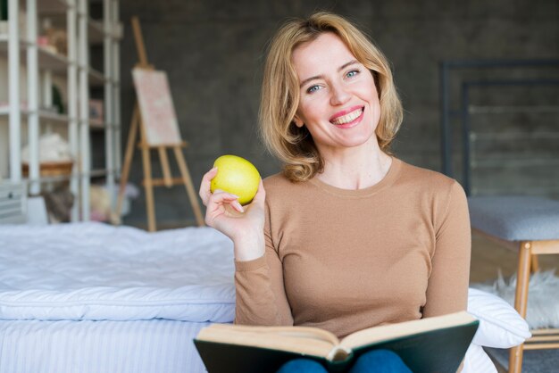 Glückliche Frau, die mit Buch und Apfel sitzt