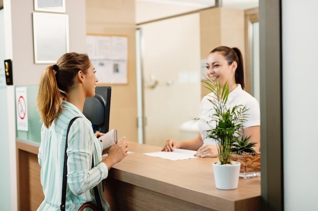 Glückliche Frau, die mit einer Empfangsdame spricht, während sie im Spa ankommt