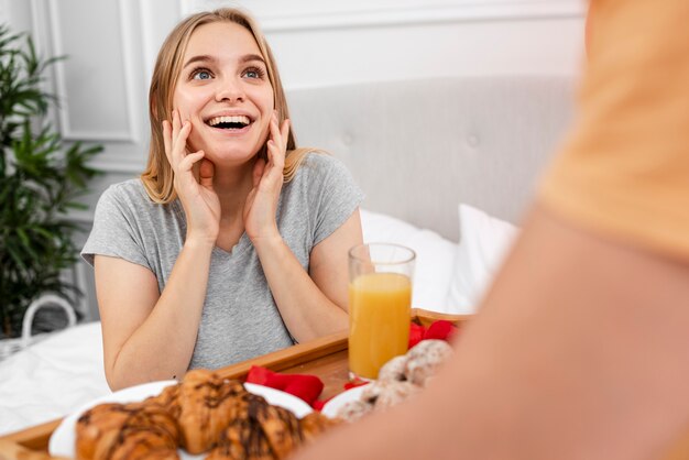 Glückliche Frau, die mit Frühstück im Bett überrascht wird