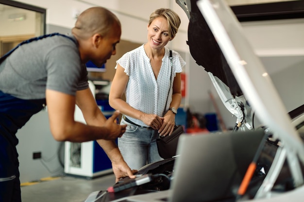 Glückliche Frau, die mit ihrem Automechaniker in einer Reparaturwerkstatt spricht