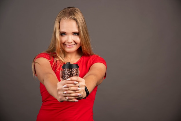 Kostenloses Foto glückliche frau, die mit kaffee zum mitnehmen auf schwarzer wand aufwirft.