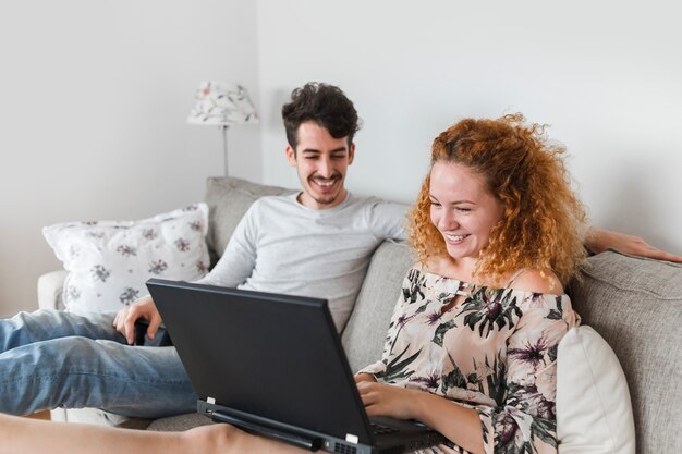 Glückliche Frau, die nahe ihrem Ehemann verwendet Laptop sitzt