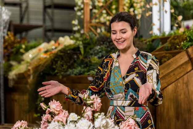 Glückliche Frau, die nahe Rosen im grünen Haus steht