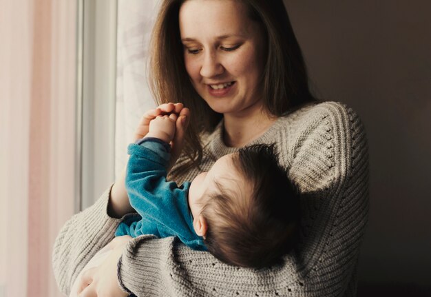 Glückliche Frau, die nettes Baby in den Armen hält