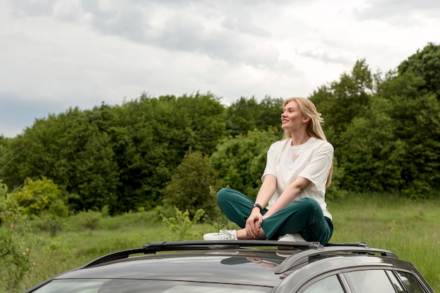 Kostenloses Foto glückliche frau, die oben auf auto in der natur aufwirft