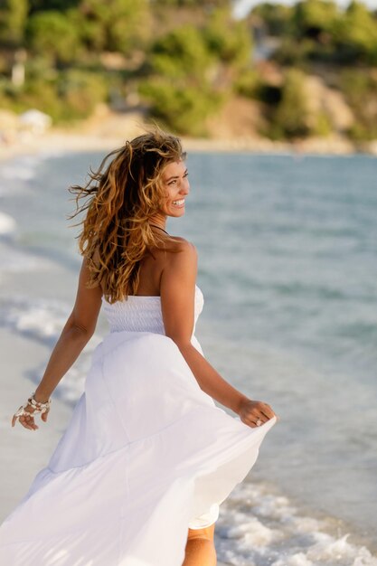 Glückliche Frau, die sich unbeschwert fühlt, während sie im Sommertag im Sommerkleid am Ufer läuft