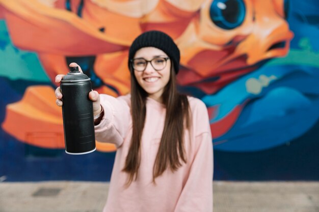 Glückliche Frau, die Sprühflasche in der Front vor Graffitiwand hält