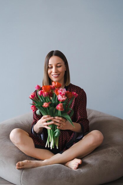 Glückliche Frau genießt einen Strauß Tulpen Hausfrau genießt einen Blumenstrauß, während sie sich auf einem bequemen Sitzsack entspannt Sweet home Allergy free