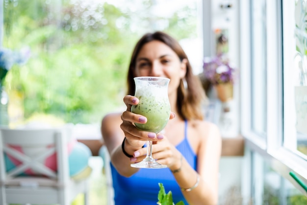 Glückliche Frau hält japanischen Matcha-Grüntee mit Eis im Glas im Café Frau mit gesundem Antioxidansgetränk im Sommer süßes Café