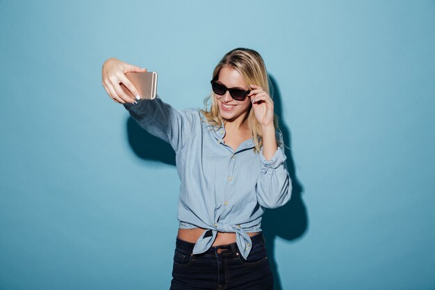 Glückliche Frau im Hemd und in Sonnenbrille, die selfie auf Smartphone machen