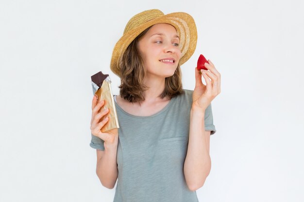 Glückliche Frau im Hut, der reife Erdbeere und Schokolade hält
