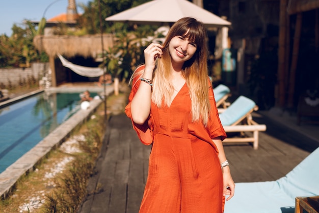 Glückliche Frau im orangefarbenen Kleid, das im tropischen authentischen Resort während der Ferien aufwirft