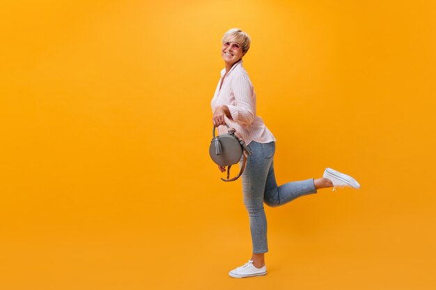 Glückliche Frau in den Jeans, die Spaß auf orange Hintergrund haben