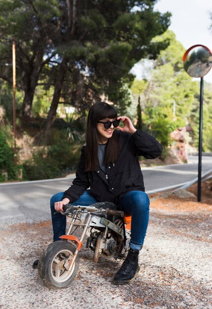 Glückliche Frau in der Sonnenbrille, die auf Minikr Motorrad sitzt