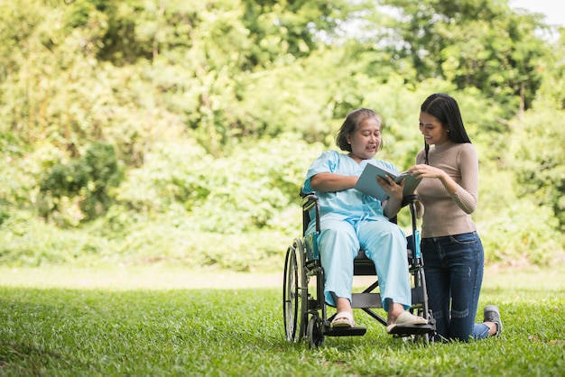 Glückliche Frau in einem Rollstuhl ein Buch mit ihrer Tochter am Park lesend