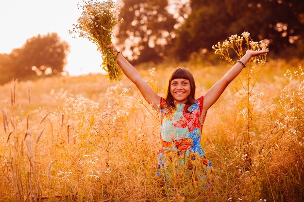 Glückliche Frau mit Blumen steht auf dem Abendfeld