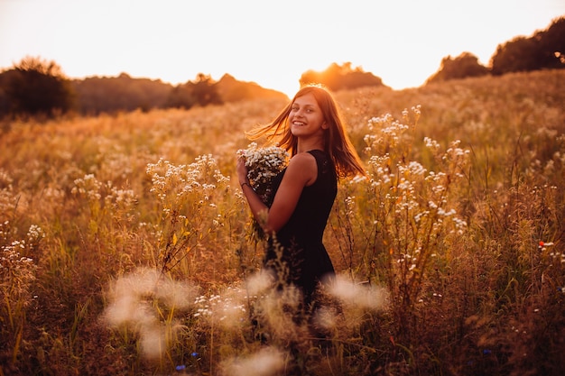 Kostenloses Foto glückliche frau mit blumen steht auf dem abendfeld