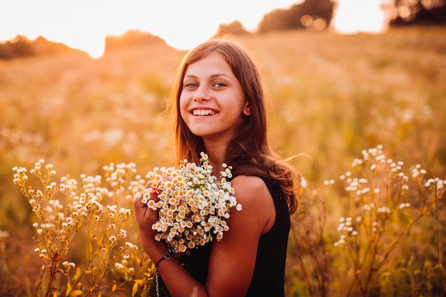 Glückliche Frau mit Blumen steht auf dem Abendfeld