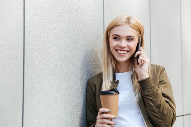 Glückliche Frau mit Kaffee, der auf Smartphone spricht