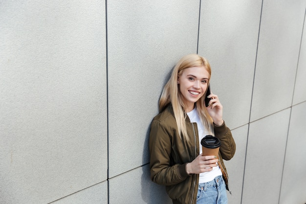 Glückliche Frau mit Kaffee, der auf Smartphone spricht