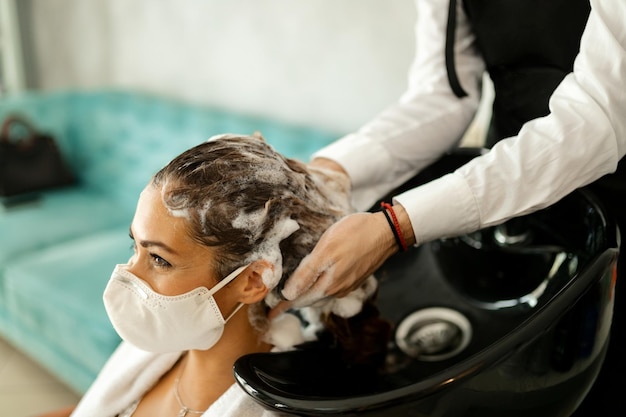 Glückliche Frau mit schützender Gesichtsmaske, die während der Coronavirus-Epidemie beim Friseur genießt