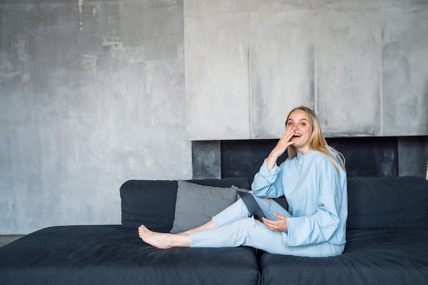 Glückliche Frau mit silbernem Laptop beim Sitzen auf dem Sofa