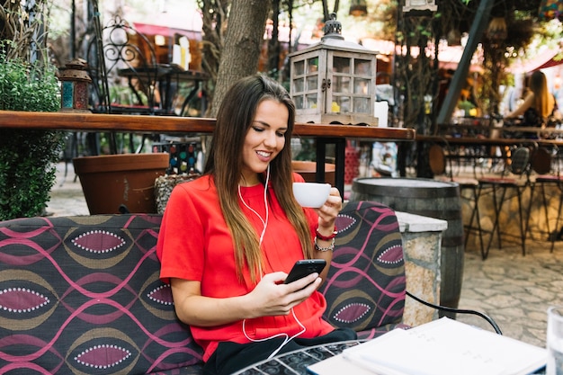 Kostenloses Foto glückliche frau mit tasse kaffee unter verwendung des mobiltelefons