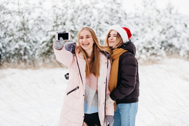 Glückliche Frauen in Sankt-Hut, der selfie im Winterwald nimmt