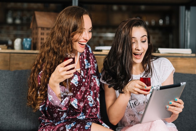 Glückliche Frauen mit Getränken unter Verwendung der digitalen Tablette