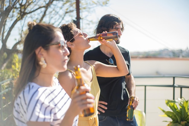 Glückliche Freunde bei Party auf dem Terrassendach. Menschen verschiedener Nationalitäten halten Bierflaschen und trinken. Party, Freundschaftskonzept
