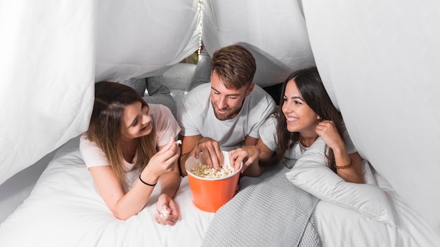 Glückliche Freunde, die auf dem Bett isst Popcorn liegen