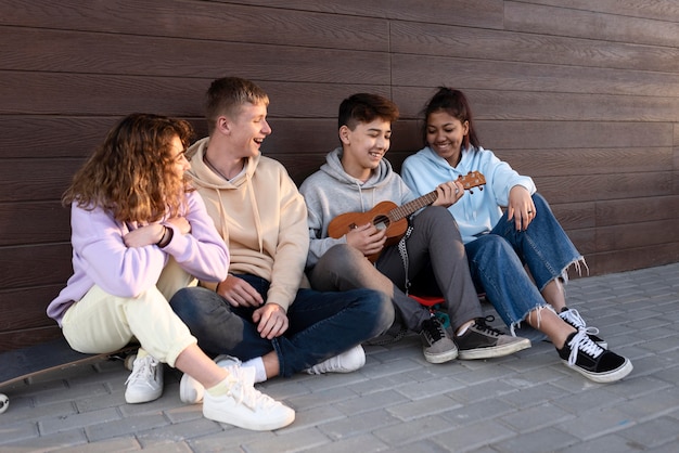 Kostenloses Foto glückliche freunde, die draußen mit ukulele sitzen