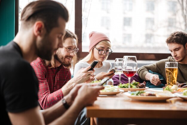 Glückliche Freunde, die im Café sitzen und Handys benutzen.