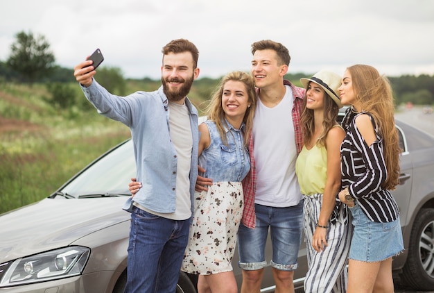 Glückliche freunde, die nahe dem auto nimmt selfie am handy stehen