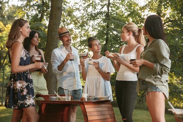 Glückliche freunde essen und trinken bier beim grillabendessen bei sonnenuntergang