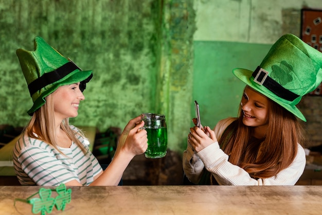 Glückliche Freundinnen feiern st. Patrick's Tag zusammen an der Bar mit einem Drink