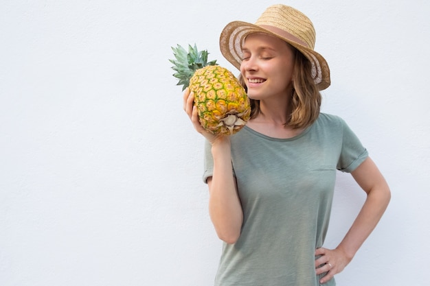 Glückliche friedliche Frau im Sommerhut, der ganze Ananas riecht