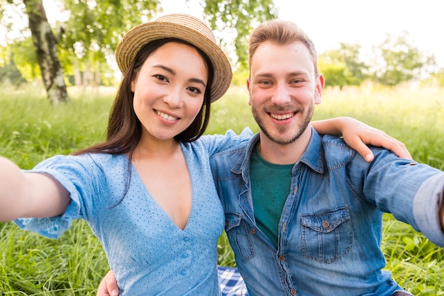 Glückliche gemischtrassige erwachsene Paare, die selfie am Park nehmen