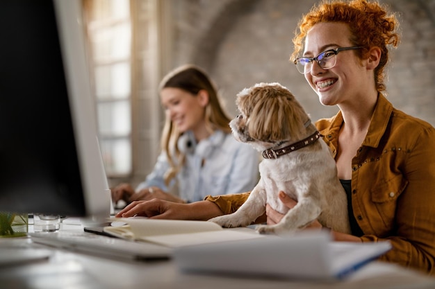 Glückliche Geschäftsfrau, die am Desktop-PC arbeitet, während sie ihren Hund im Büro hält