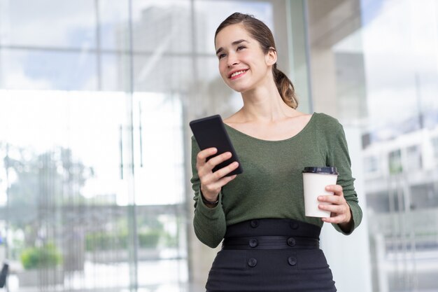 Glückliche Geschäftsfrau, die mit Handy und Kaffee steht