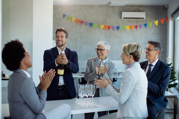 Kostenloses Foto glückliche geschäftsleute, die eine flasche champagner öffnen, während sie auf einer büroparty feiern
