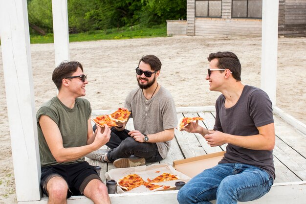 Glückliche Gesellschaft, die Pizza auf Picknick plaudert und isst