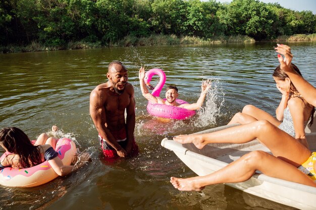 Glückliche Gruppe von Freunden, die Spaß beim Lachen und Schwimmen im Fluss haben