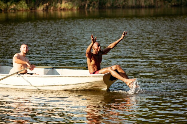 Glückliche Gruppe von Freunden, die Spaß haben, während sie lachen, Wasser spritzen und im Fluss schwimmen