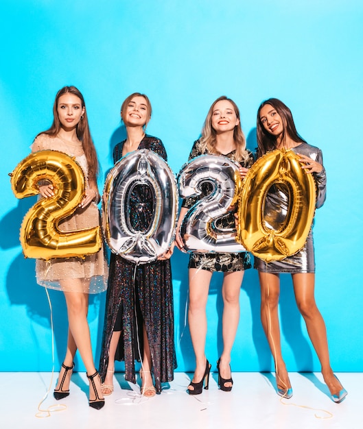 Glückliche herrliche mädchen in den stilvollen sexy party-kleidern, die gold und silber 2020 ballone halten